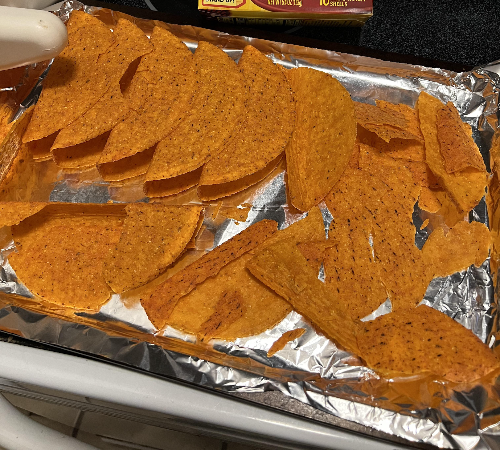 Orange taco shells arranged on a foil-lined baking sheet.