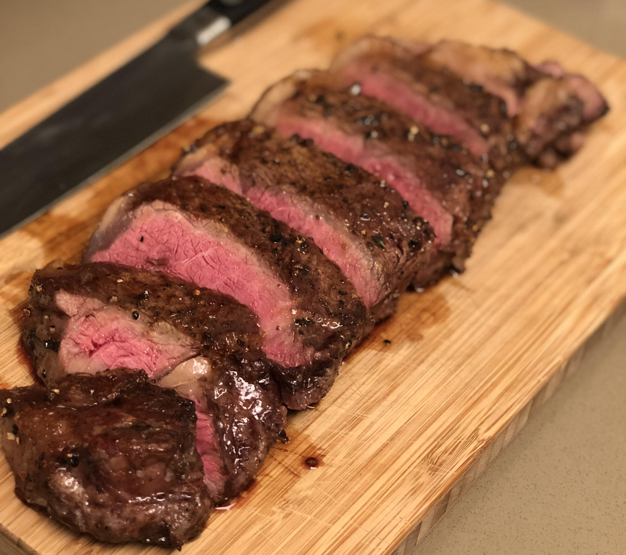 Slices of medium-rare steak on a wooden cutting board with a knife in the background.