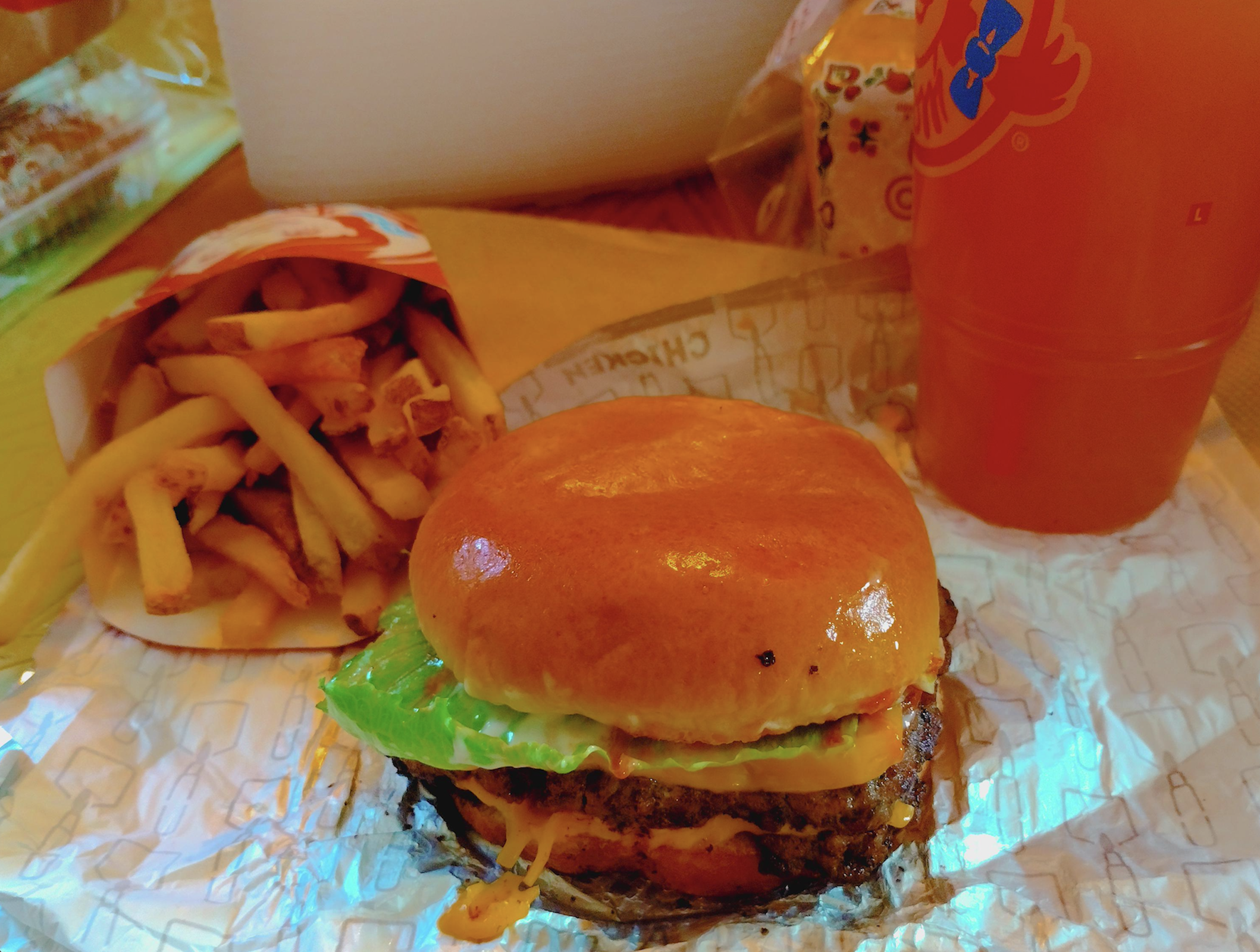 A cheeseburger, a container of french fries, and a large orange soda on a tray.