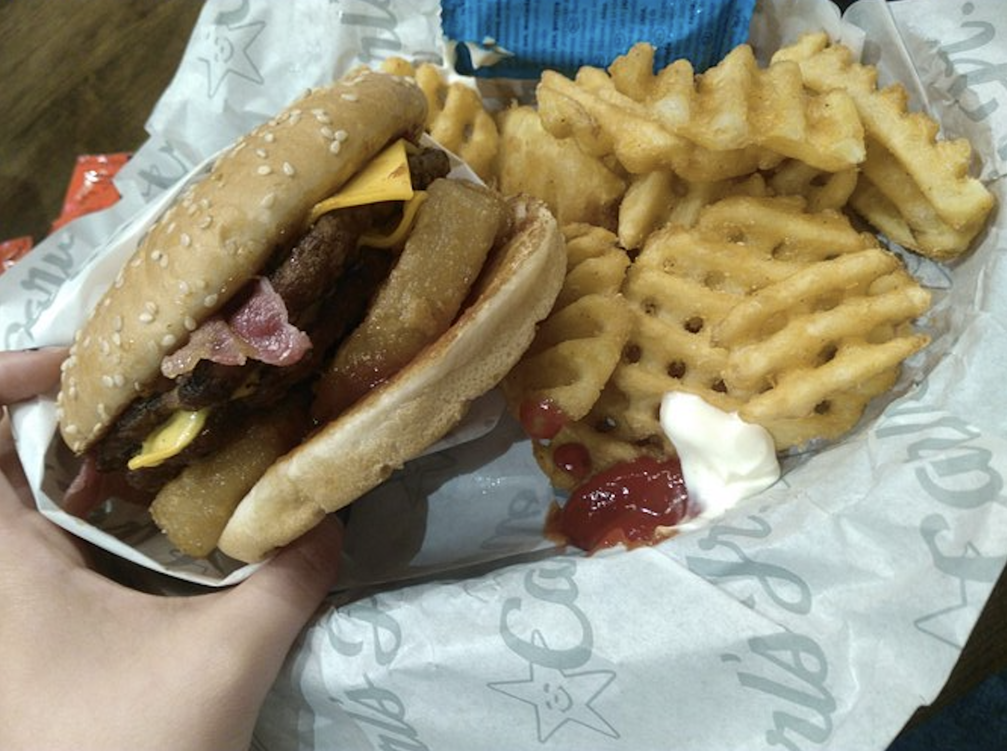 A double cheeseburger with an onion ring and bacon next to a side of waffle fries with ketchup and mayonnaise.