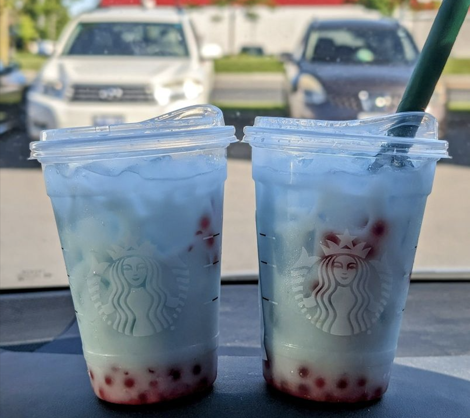 Two clear Starbucks plastic cups containing a light blue iced beverage with red boba pearls at the bottom.