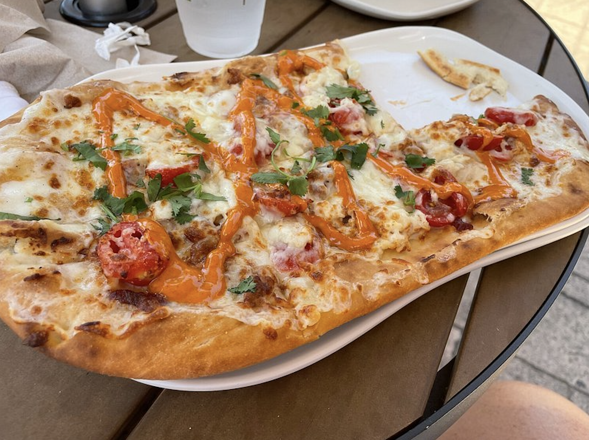 Flatbread pizza, one of Panera's fast-food menus, topped with melted cheese, cherry tomatoes, fresh herbs, and a spicy orange drizzle on a white rectangular plate.