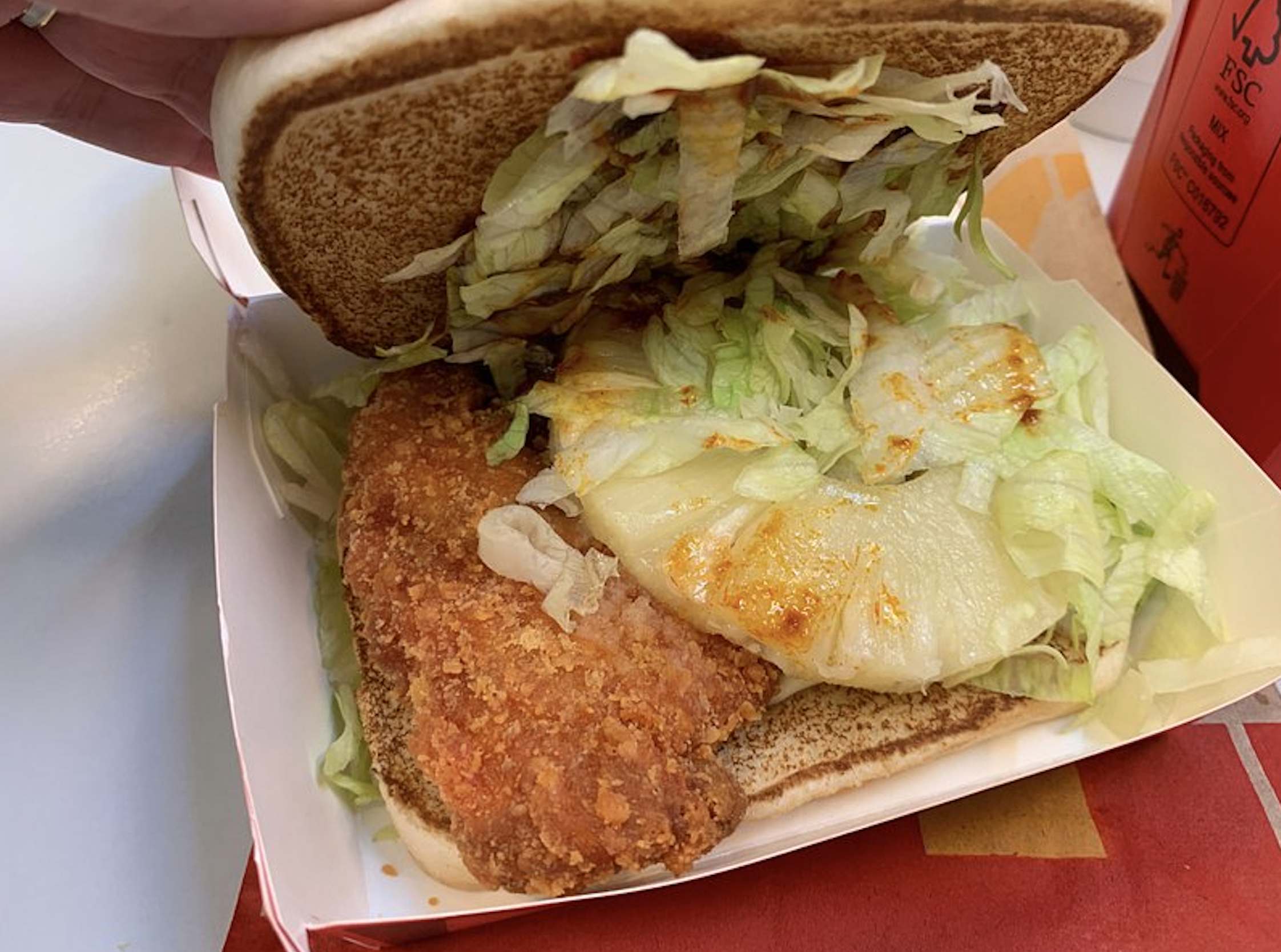 A fried chicken sandwich in a cardboard container, opened to show a piece of fried chicken, a pineapple slice, and shredded lettuce.