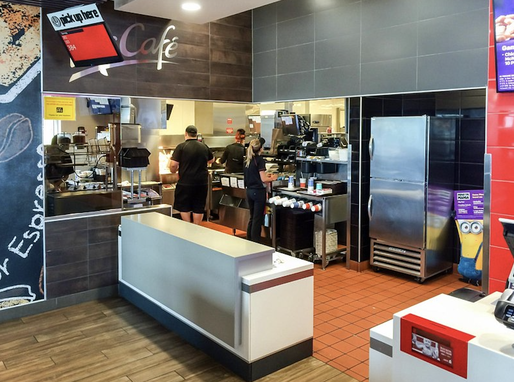 Employees work in the open kitchen of a cafe with a “pick up here” sign hanging above the counter.