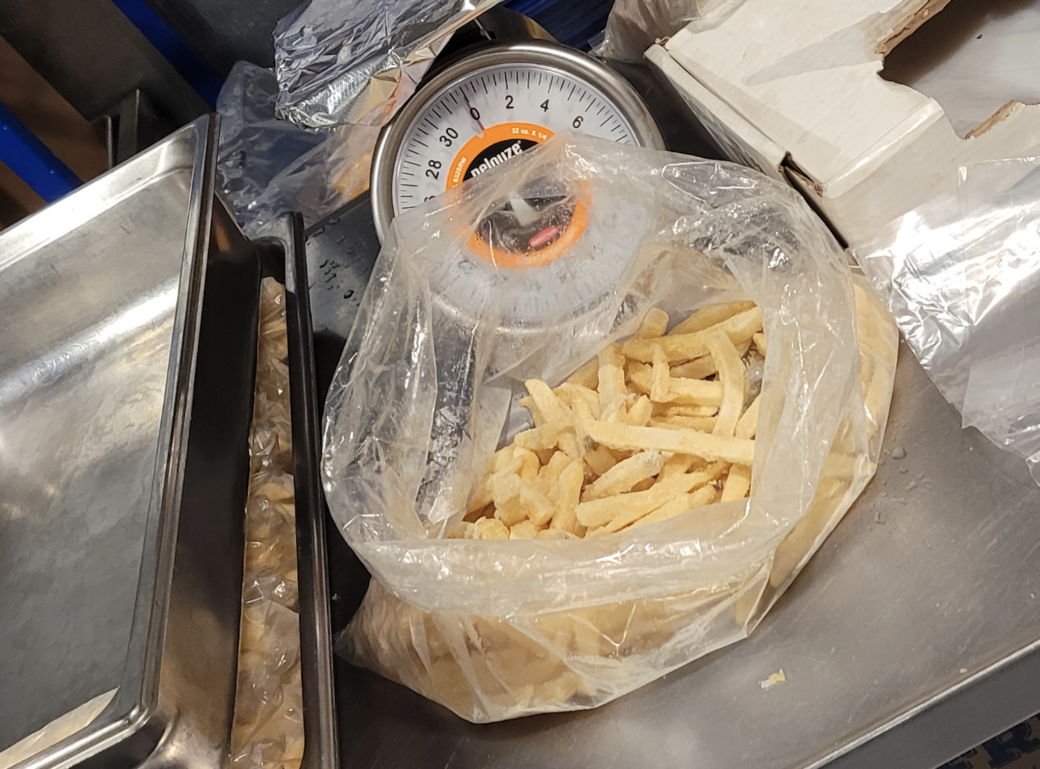 A bag of frozen french fries sits on a metal scale next to a stainless steel tray.