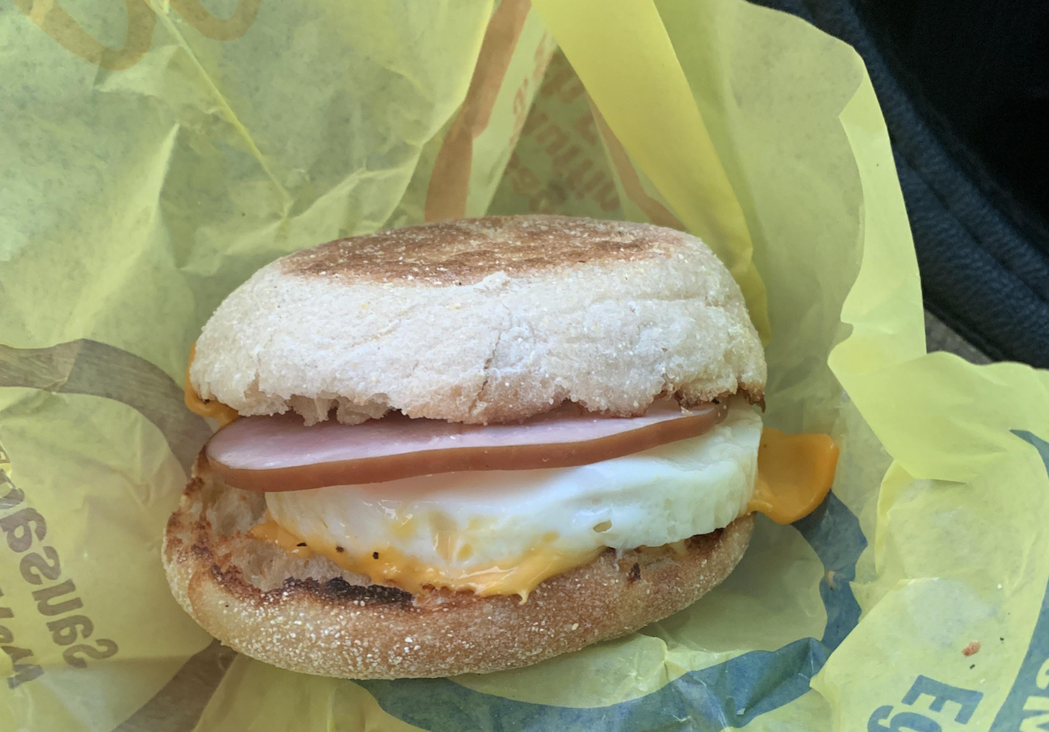 An egg and Canadian bacon breakfast sandwich on an English muffin, wrapped in yellow paper.