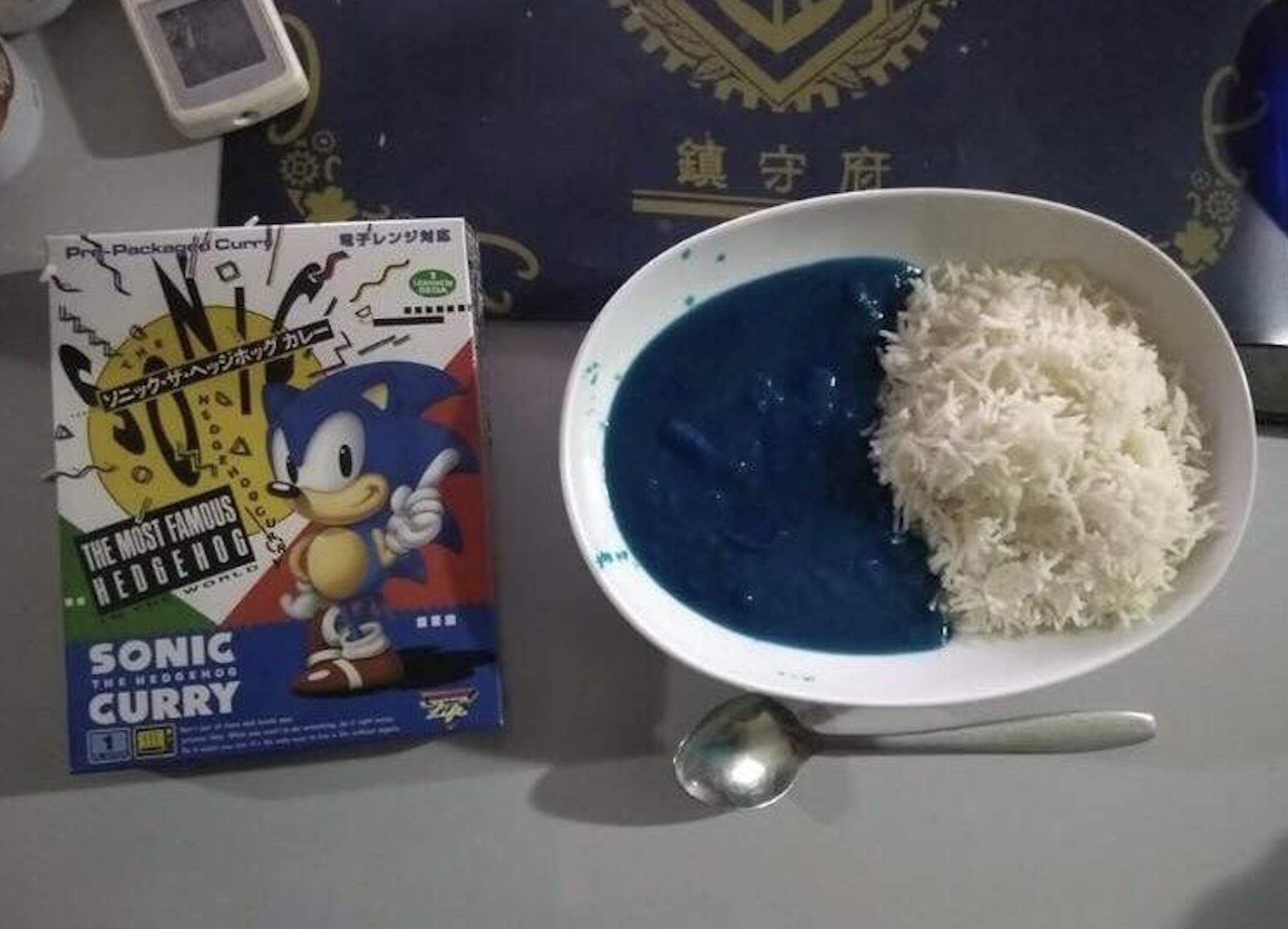 A box of Sonic the Hedgehog instant curry next to a bowl of white rice served with a side of bright blue curry sauce.