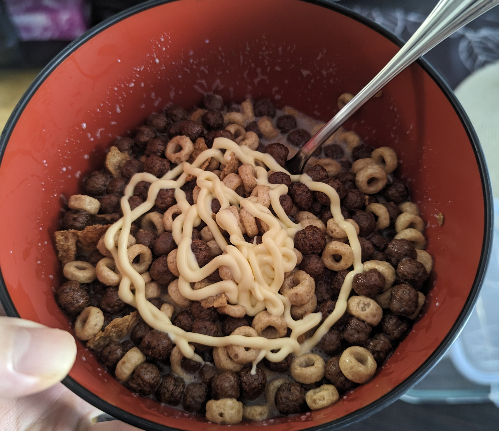 A bowl of chocolate and oat cereal in milk, drizzled with a swirl of mayonnaise and served with a spoon that it's one of the weird food combinations.