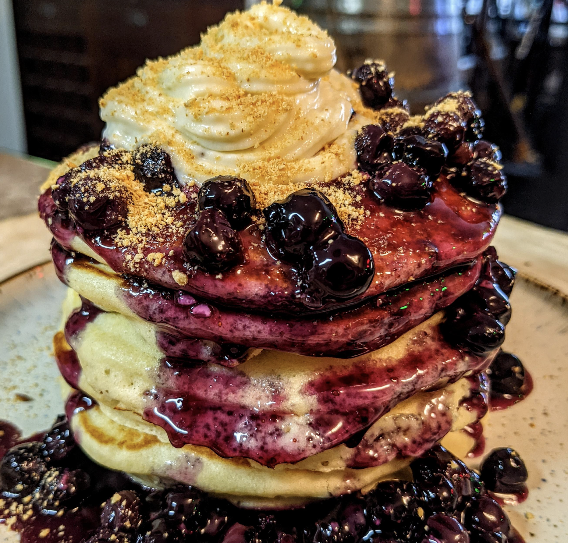 Stack of pancakes topped with a swirl of whipped cream, blueberry compote, and crumbled graham crackers.