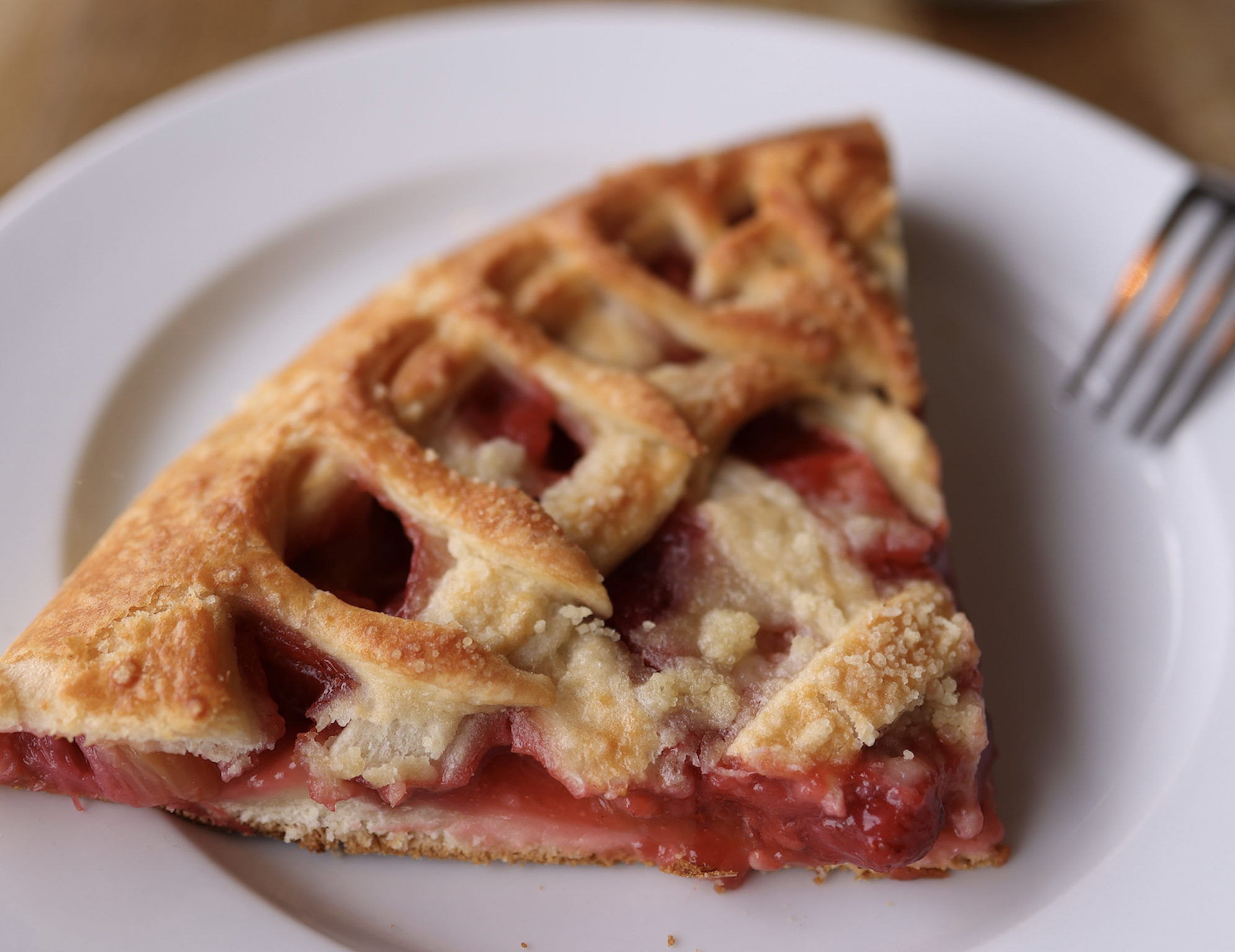A slice of lattice-topped fruit pie on a white plate with a fork nearby.