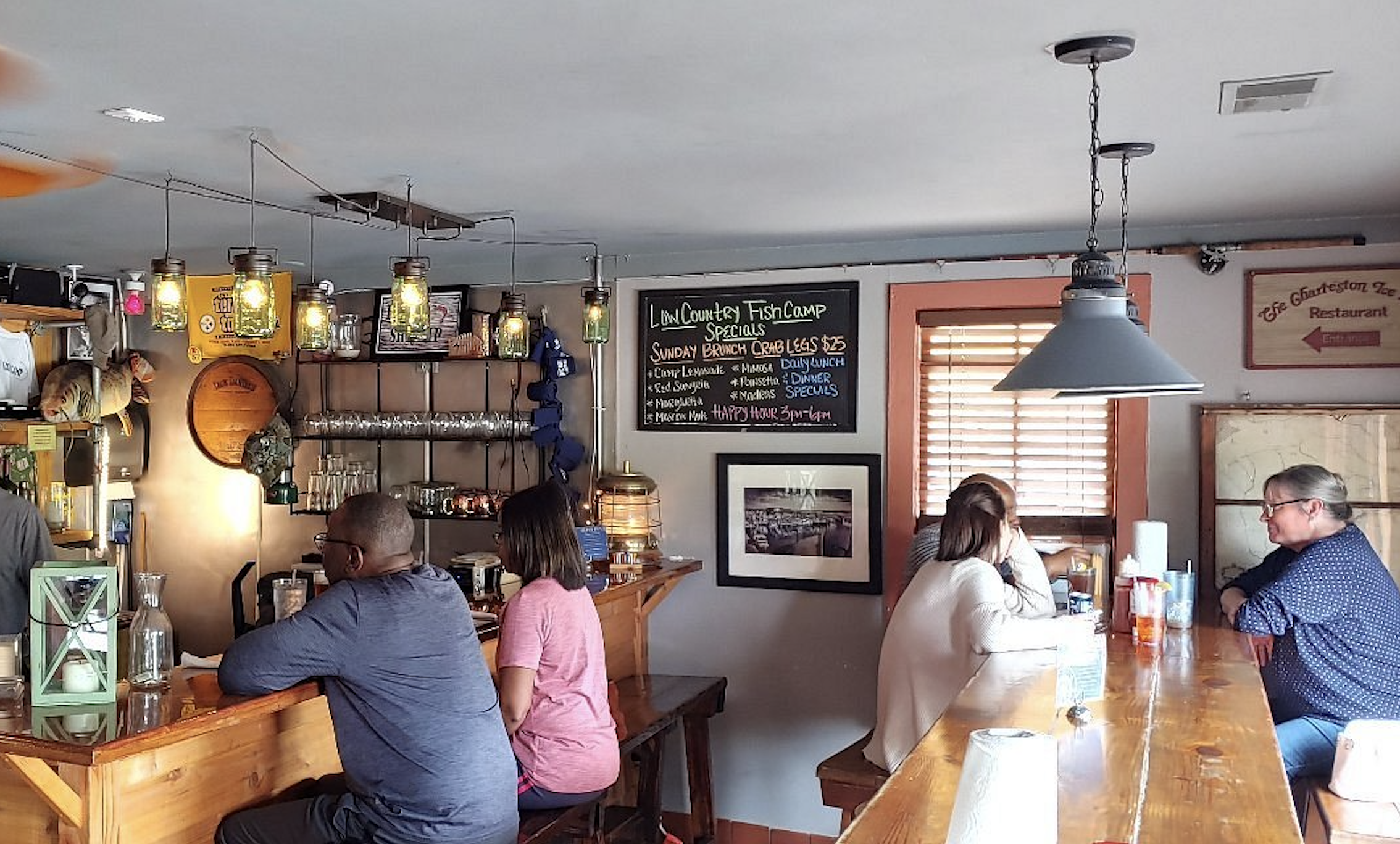 Patrons sit at a wooden bar in a restaurant, with a chalkboard menu listing specials on the wall, as regional restaurant traditions indicates.
