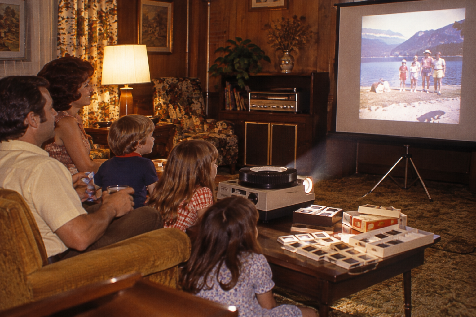 A family sits in a living room watching a vacation slide show projected onto a screen. Family activities before screens.