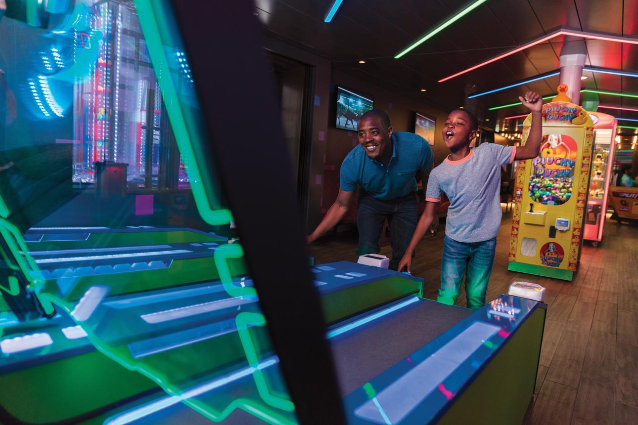 A man and a boy playing an arcade game together among the cruise ship amenities.