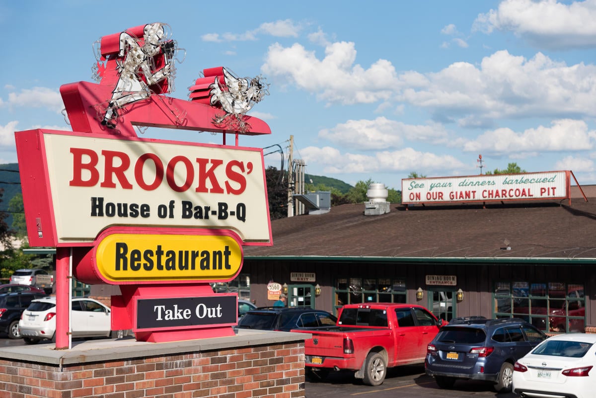 A large roadside sign for Brooks’ House of Bar-B-Q restaurant, with the restaurant building and parking lot in the background.