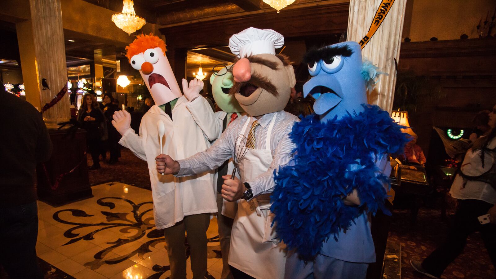 Four people wearing Muppet costumes of Beaker, Dr. Bunsen Honeydew, the Swedish Chef, and Sam the Eagle stand in an indoor event space.