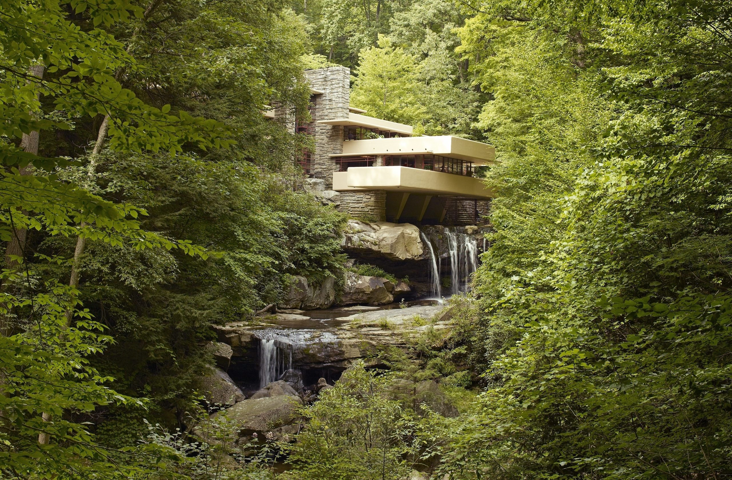 Fallingwater house built over a tiered waterfall in a wooded forest.