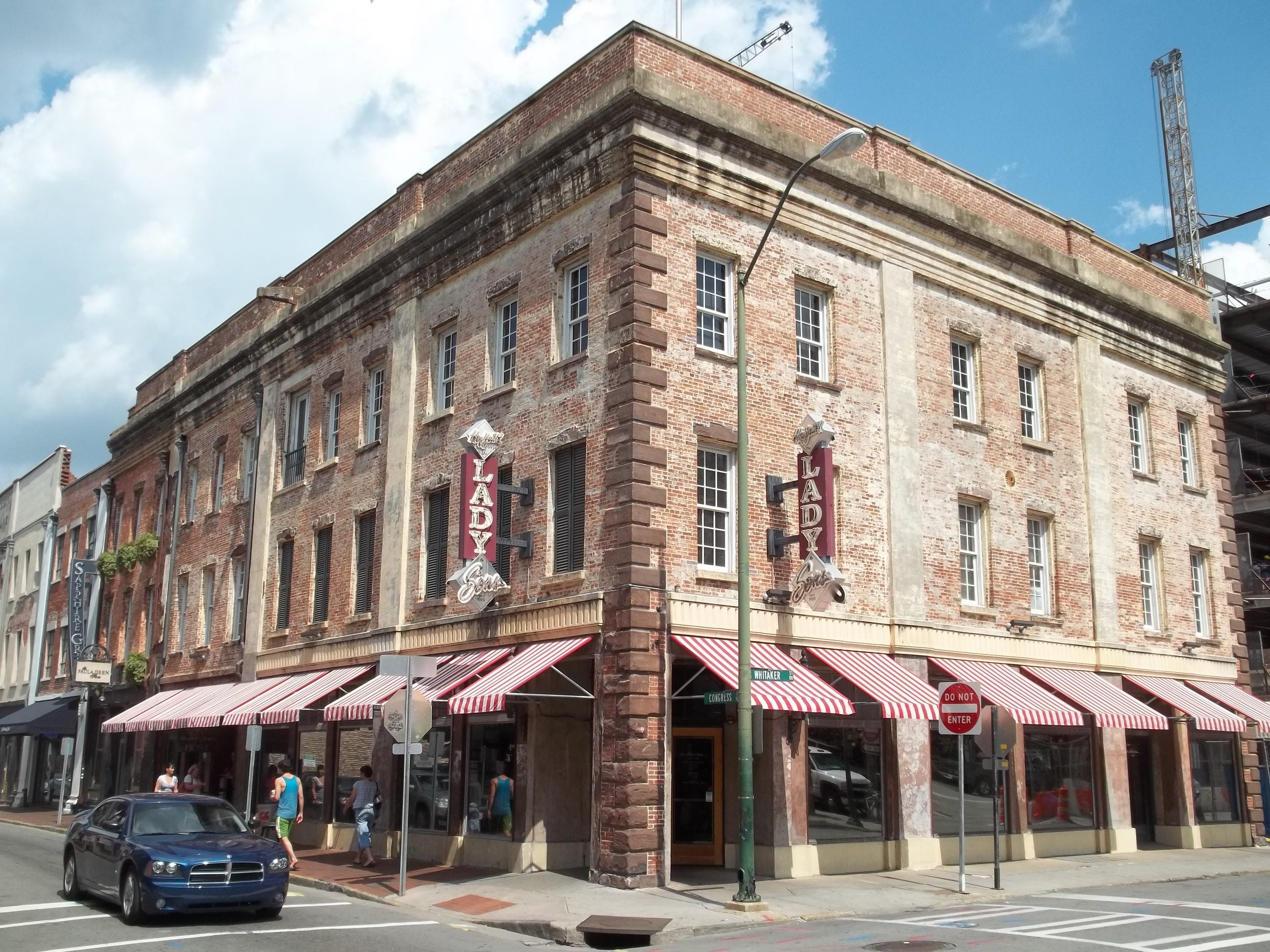 A three-story historic brick building with red-striped awnings, large windows, and two signs reading “LADY,” anchors the corner of One Great Neighborhood—perfect for trips where local charm shines.