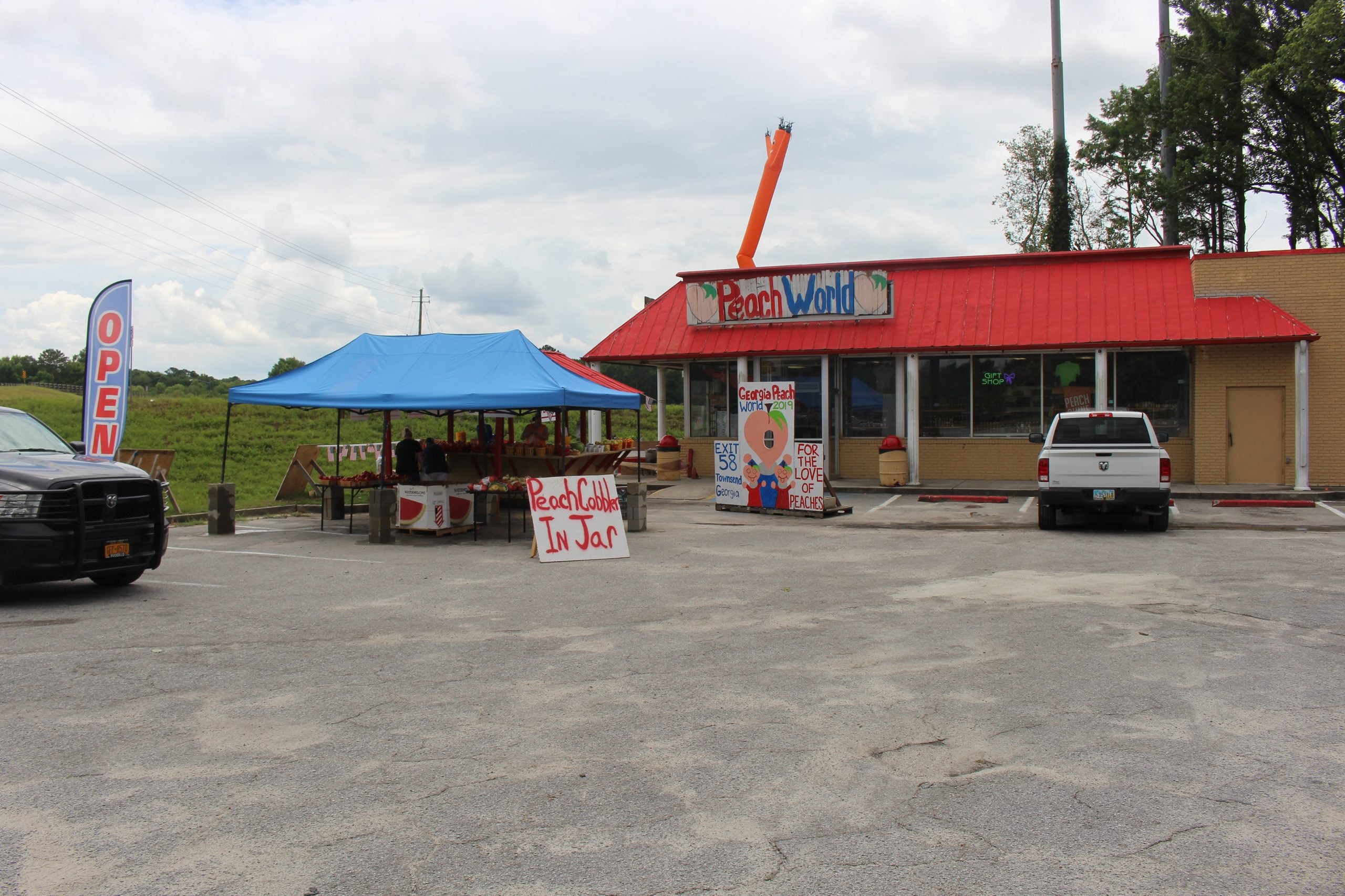 Peach World store with a blue vendor tent in the parking lot and a sign advertising “Peach Cobbler In Jar” for your next food trip.
