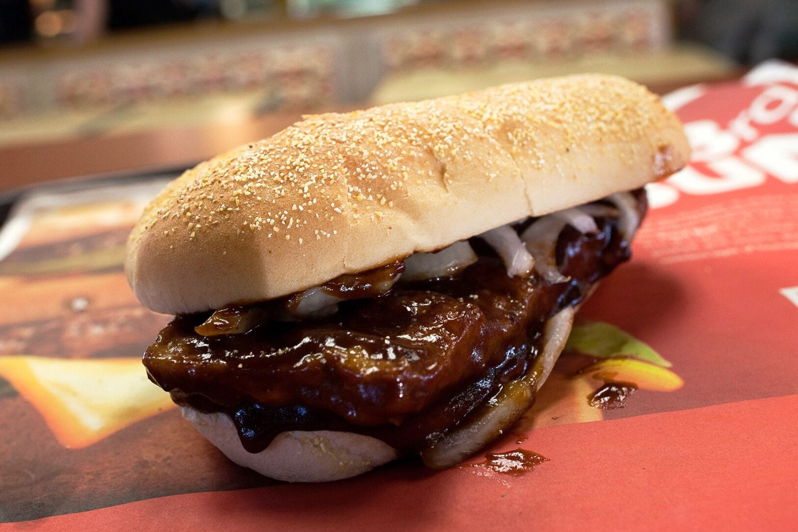 A boneless rib sandwich topped with sliced onions on a seeded bun.