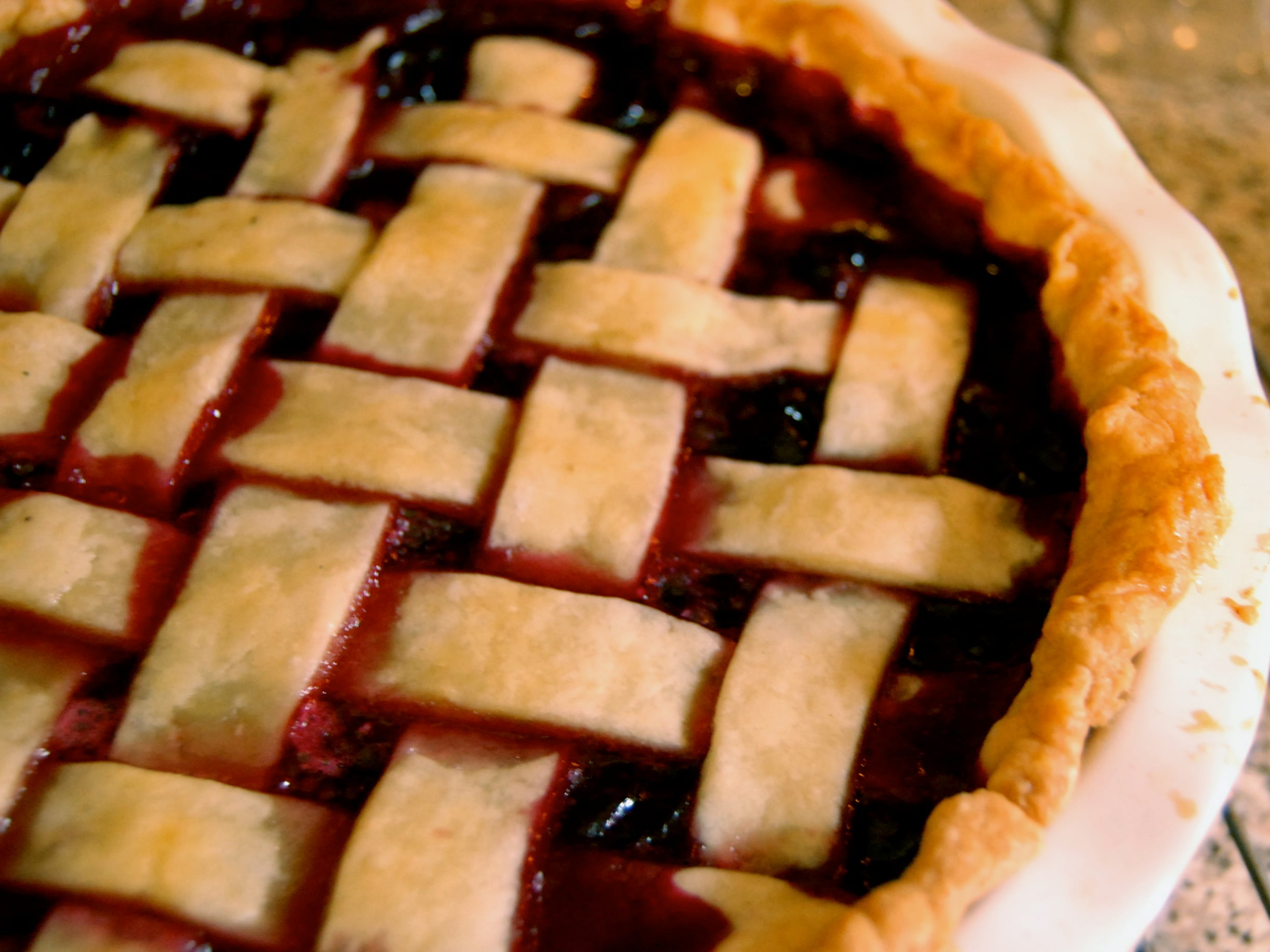 A berry pie with a golden-brown lattice crust in a white ceramic dish, perfect for food trips.