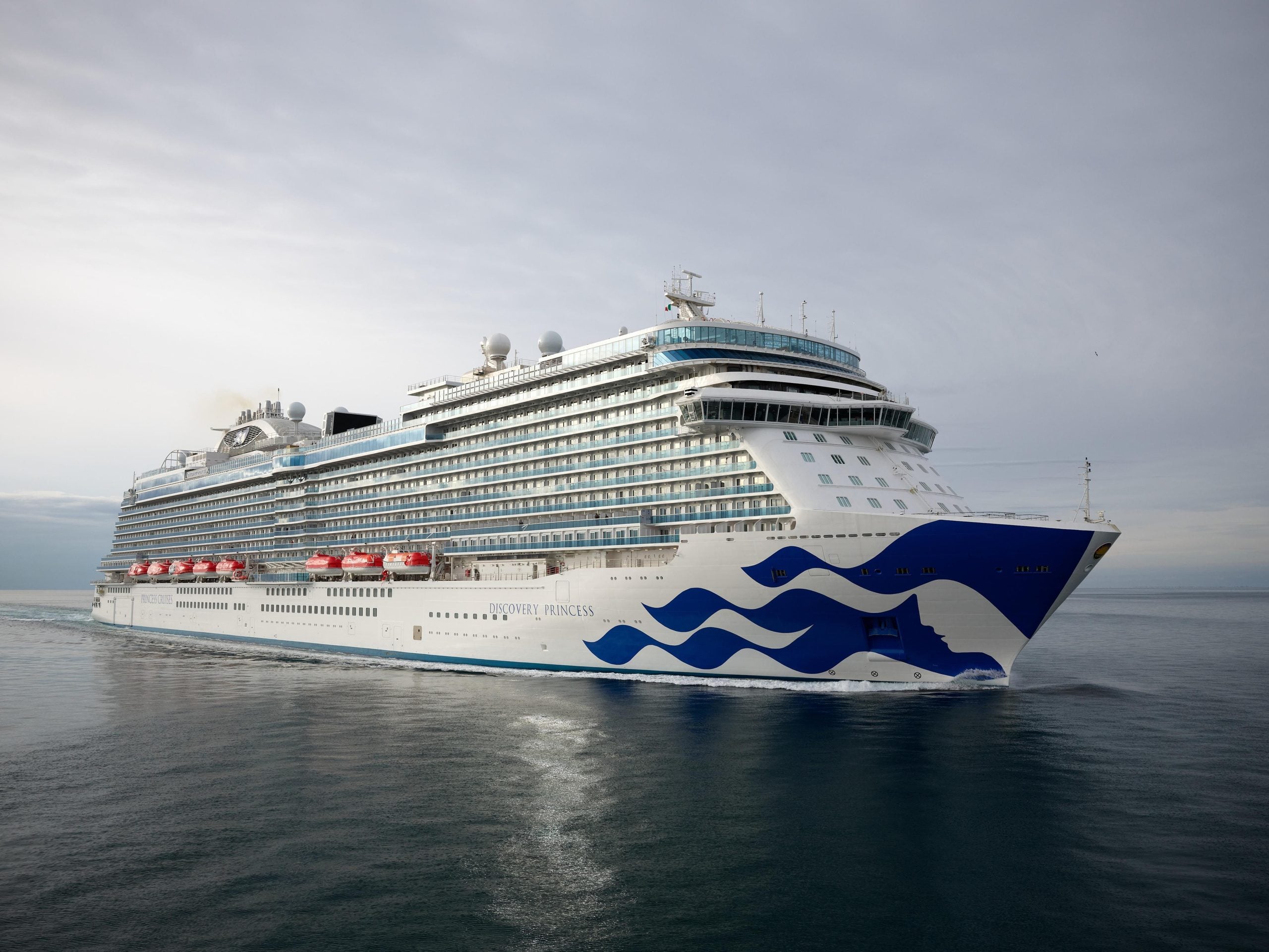The Discovery Princess cruise ship sailing across calm water, passing near the decks where guests enjoy the cruise ship buffets.