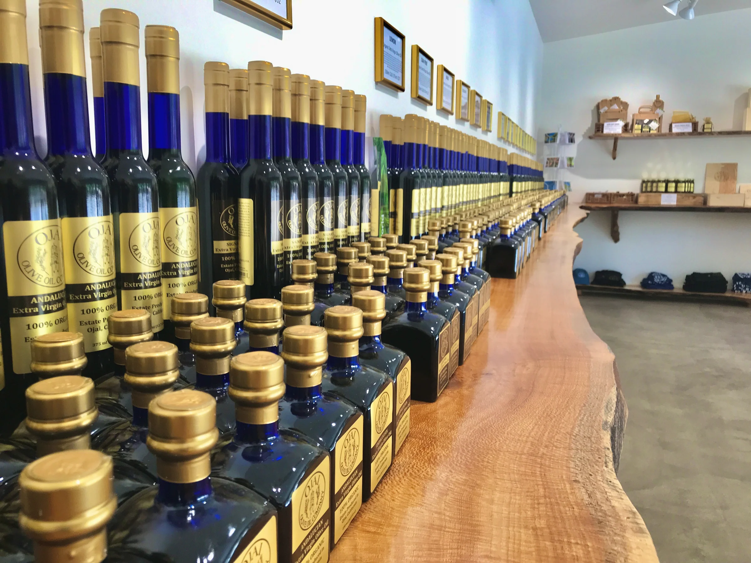 Rows of blue glass bottles of Ojai extra virgin olive oil, a best souvenir, displayed on a long wooden slab counter.