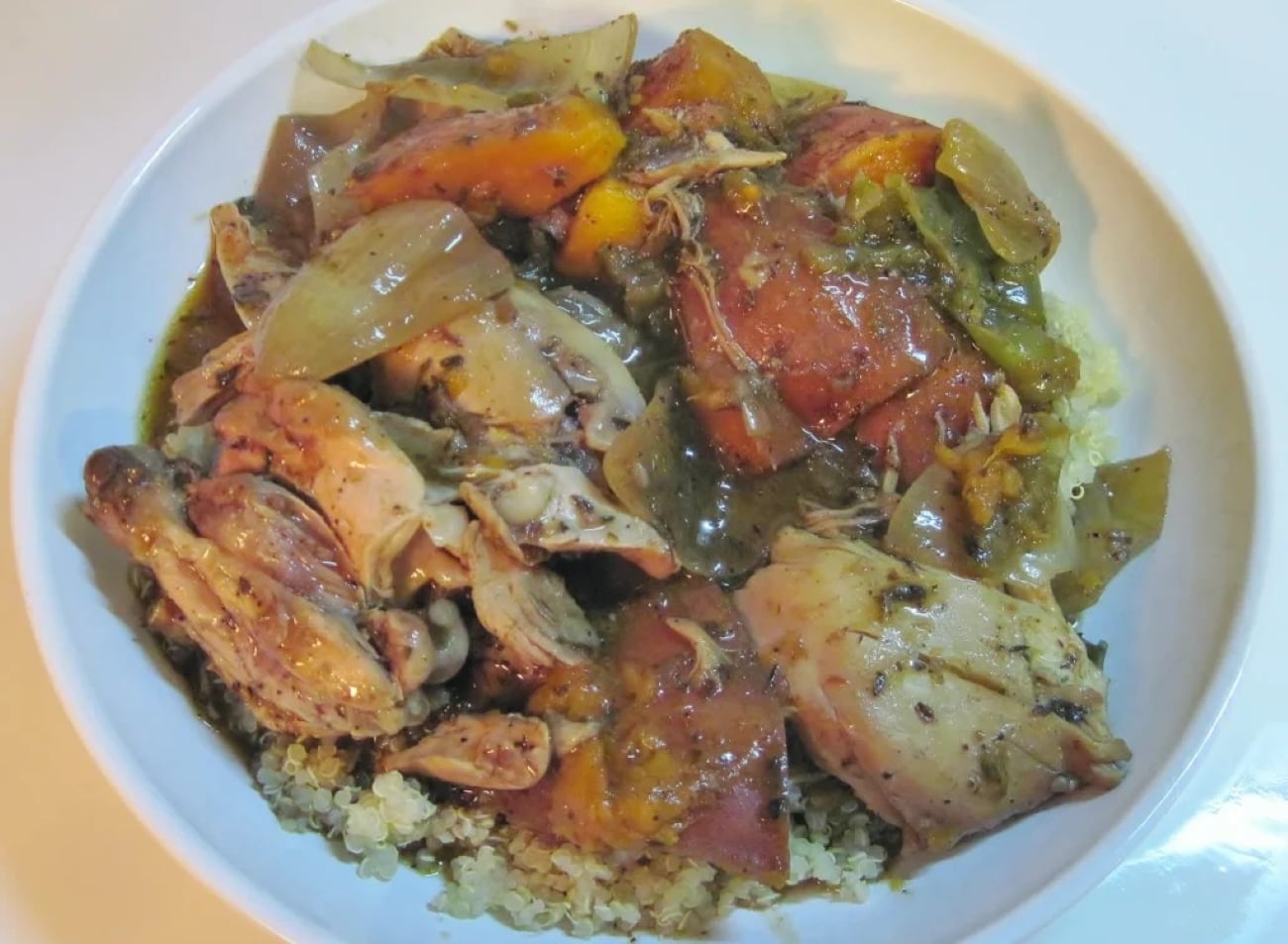 A bowl of braised chicken pieces with chunks of roasted squash and onions served over a bed of quinoa.