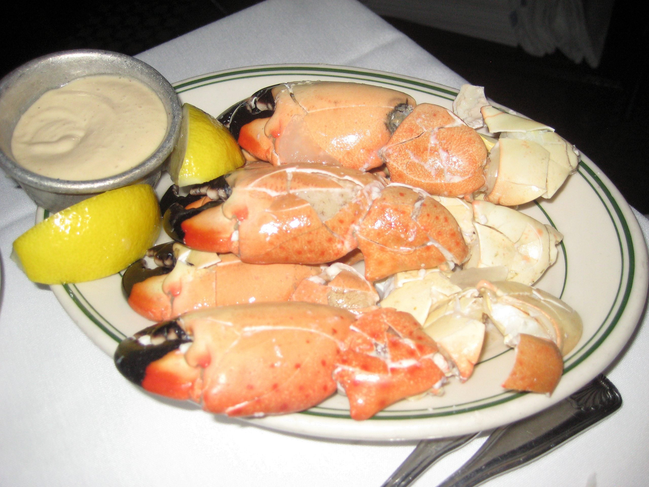 A plate of stone crab claws served with two lemon wedges and a side of dipping sauce.