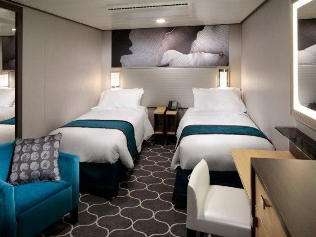 cruise ship cabins A cruise ship cabin with two twin beds, a teal armchair, a small desk with a white chair, and patterned carpeting.