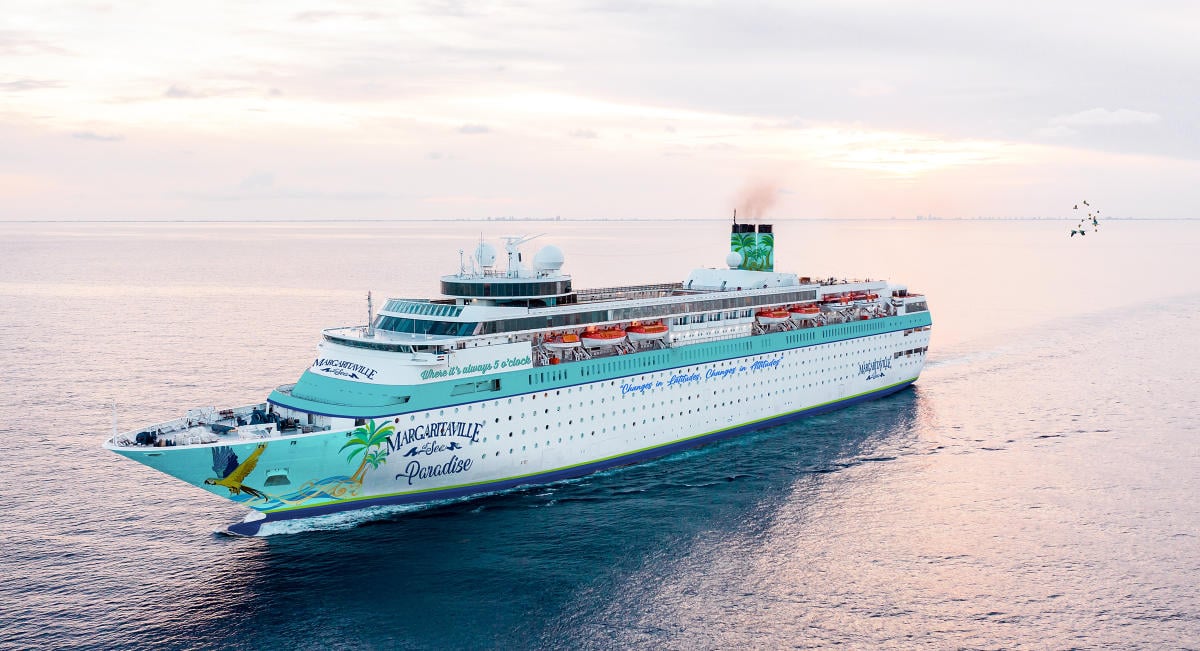 A Margaritaville at Sea cruise ship sailing on the ocean during sunset, past the windows of its onboard cruise ship buffets.