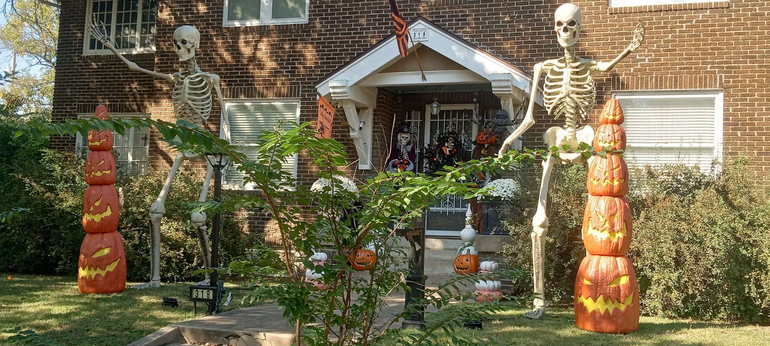 Two large skeletons stand on either side of a house entrance, each flanked by a stack of three illuminated jack-o’-lanterns.