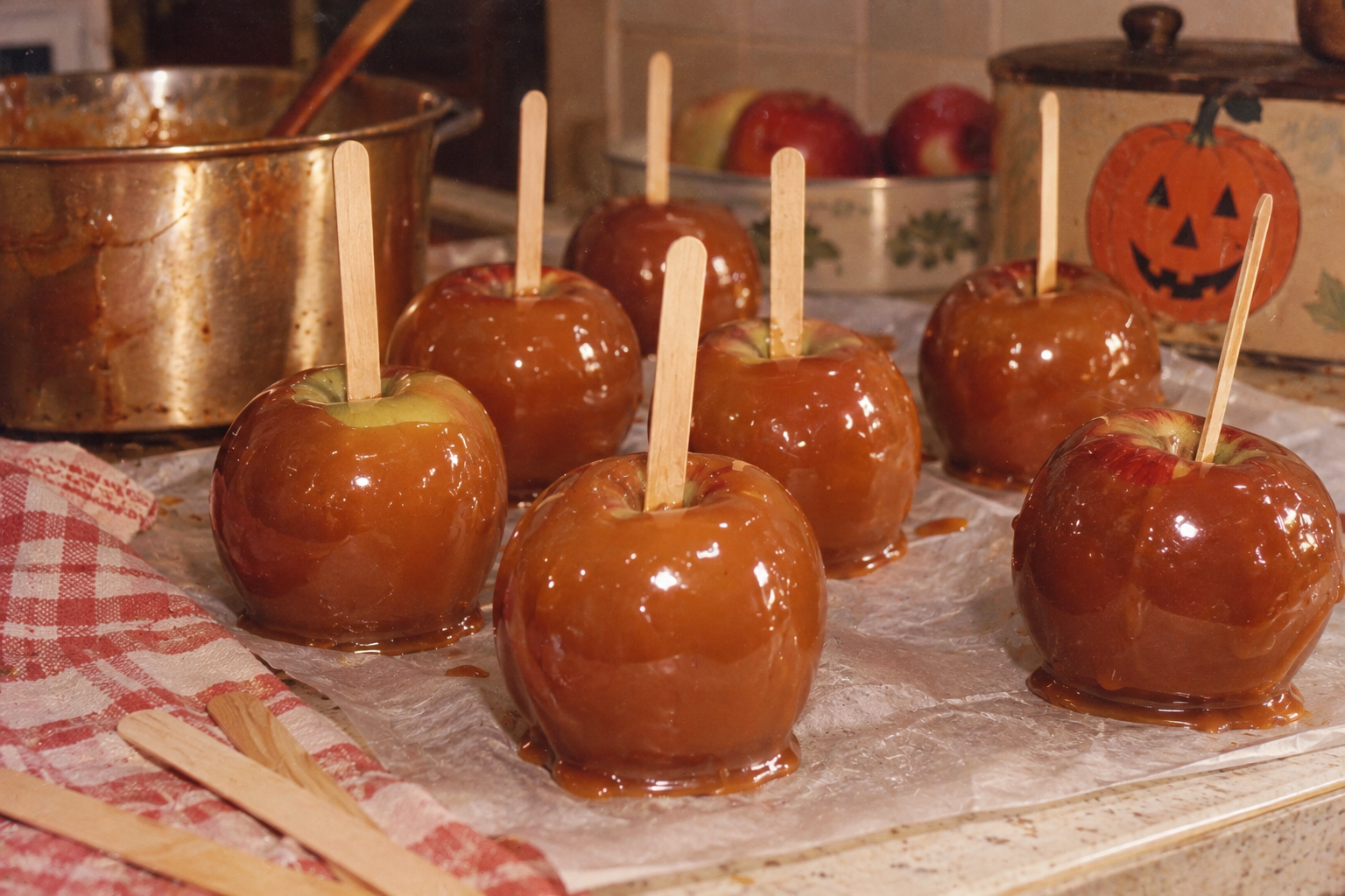 Six caramel apples with wooden sticks resting on parchment paper.
