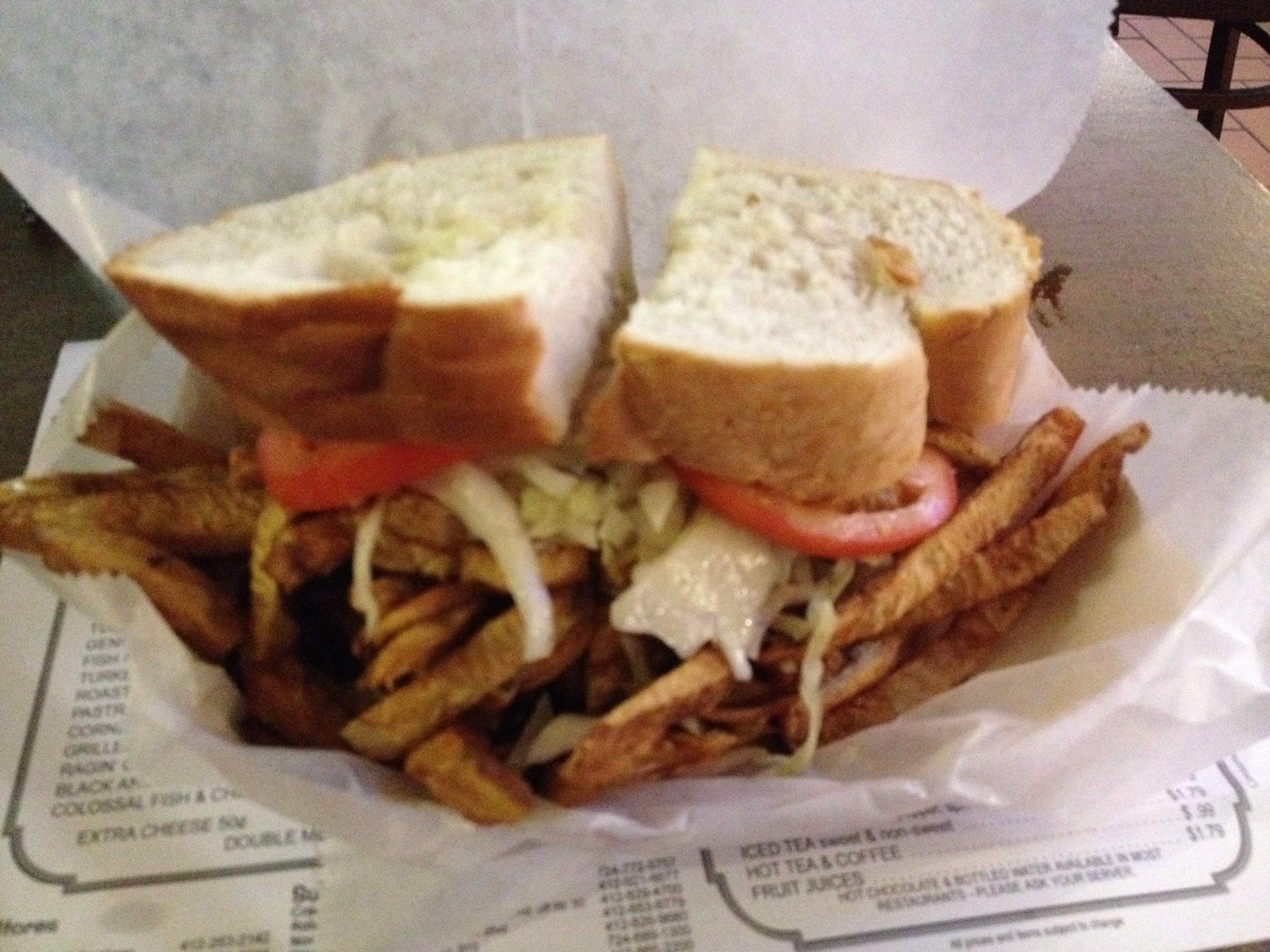 A sandwich on white bread filled with meat, coleslaw, and tomatoes, served in a basket with a side of french fries.