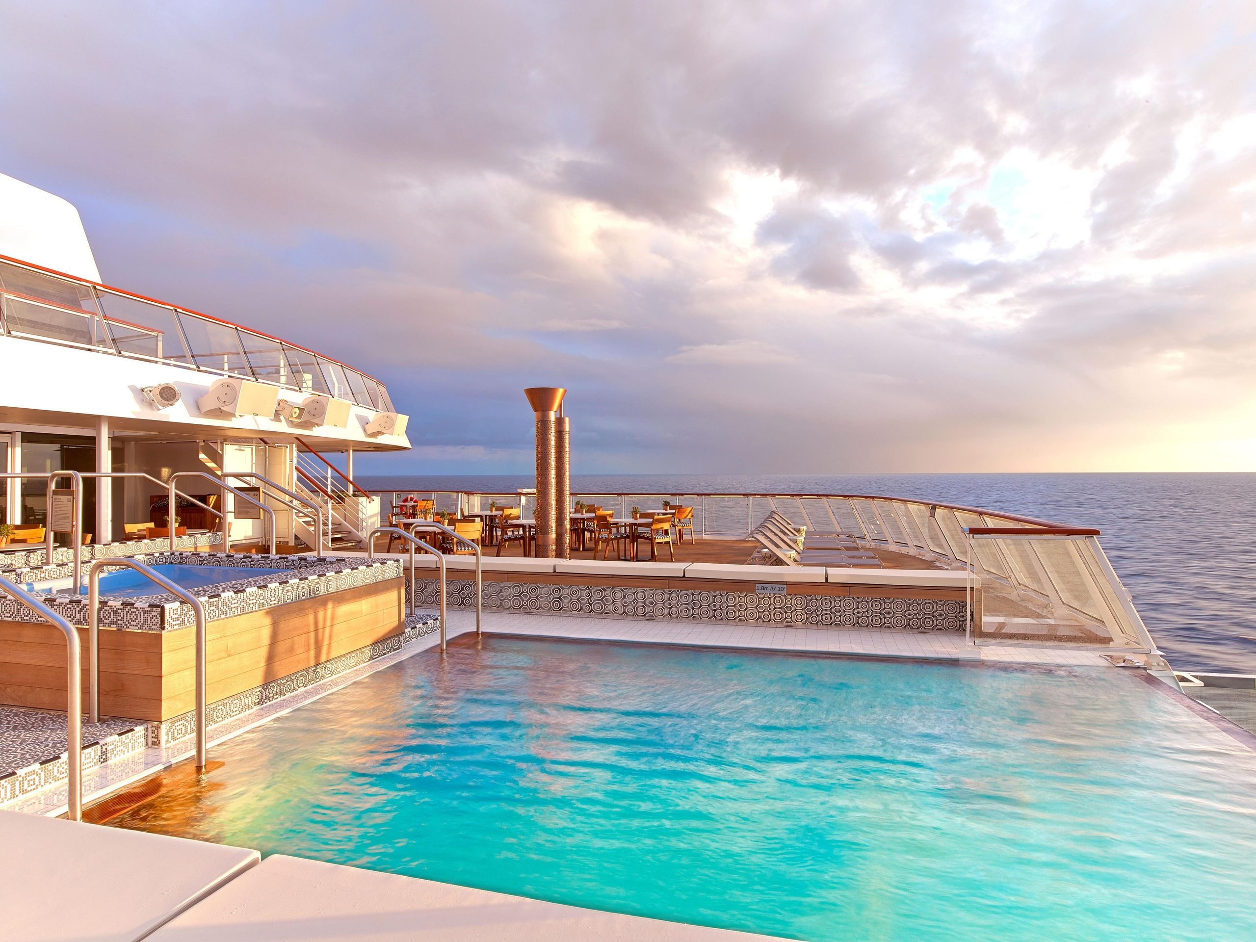 An infinity pool and hot tub on the deck of a cruise ship overlooking the ocean at sunset.