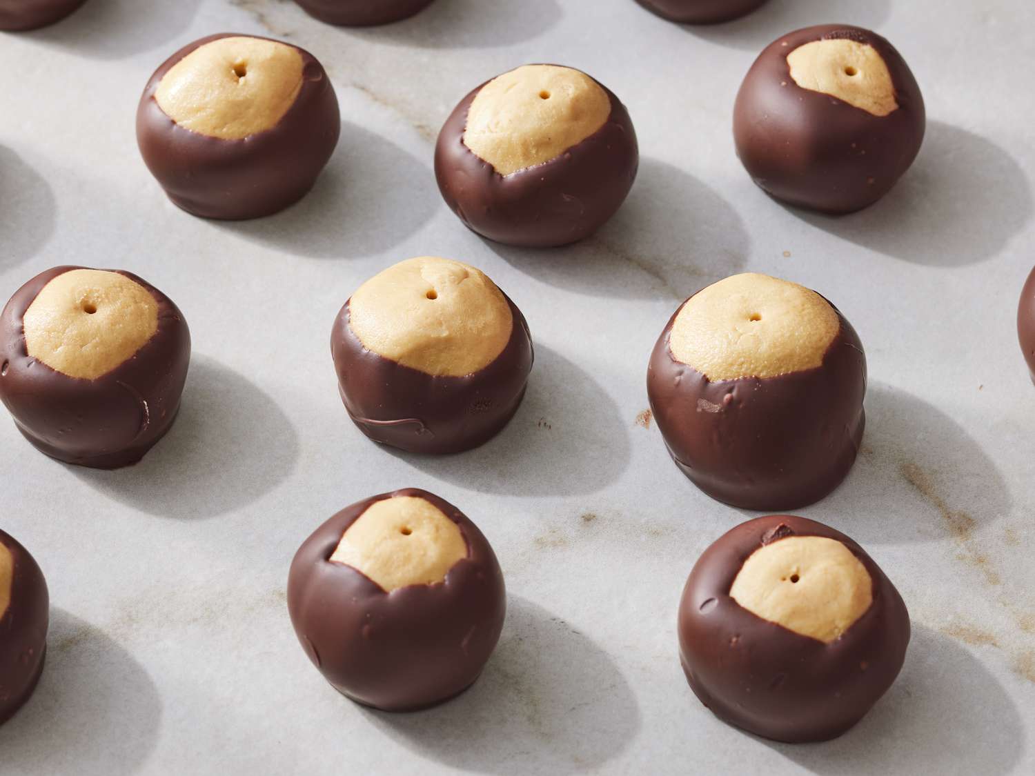 Several buckeye candies, a classic among regional desserts, consist of peanut butter balls partially dipped in dark chocolate and arranged on a marble surface.