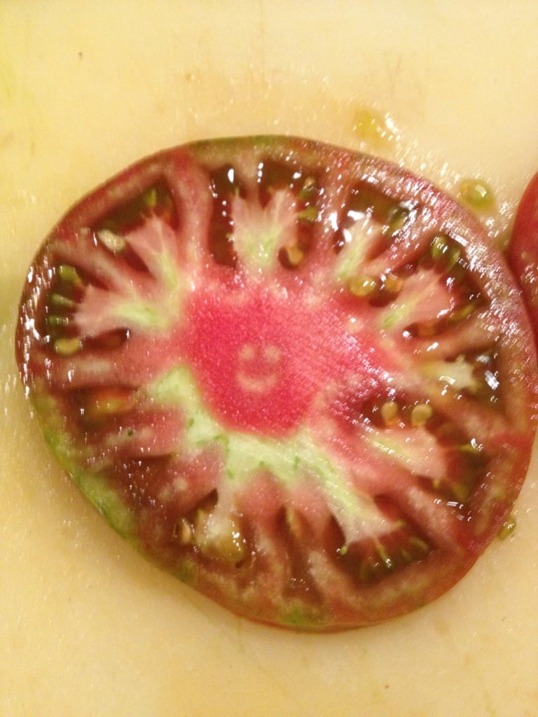 A cross-section slice of a tomato with a natural smiley face pattern in the center.