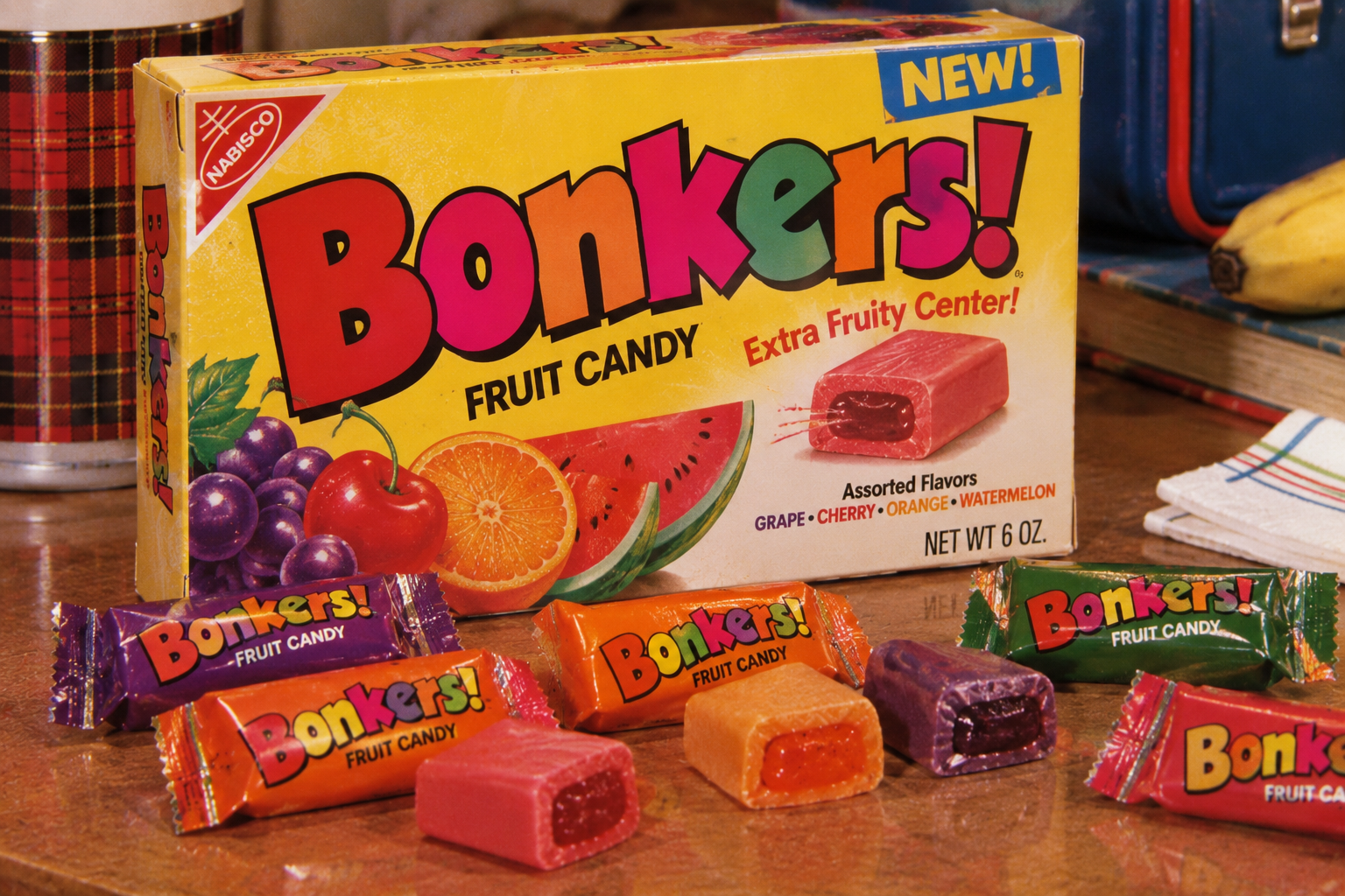 A colorful Bonkers! Fruit Candy box with grape, watermelon, cherry, and orange candies unwrapped in front. The packaging highlights “Extra Fruity Center!” and features vibrant fruit illustrations.