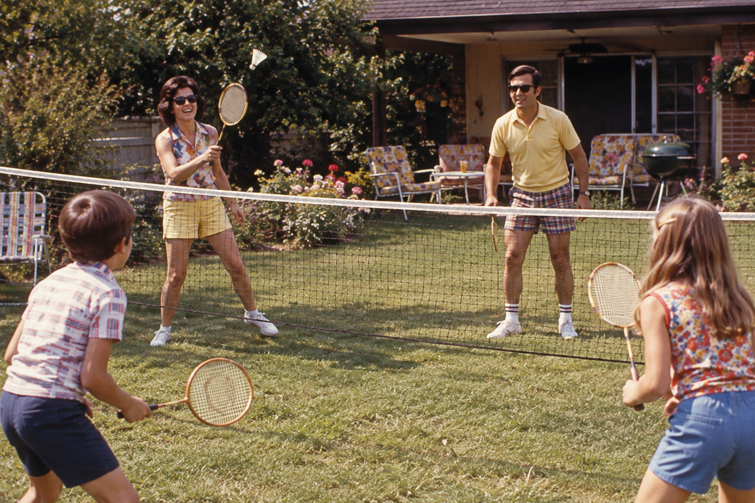 A family of four playing badminton in a backyard.