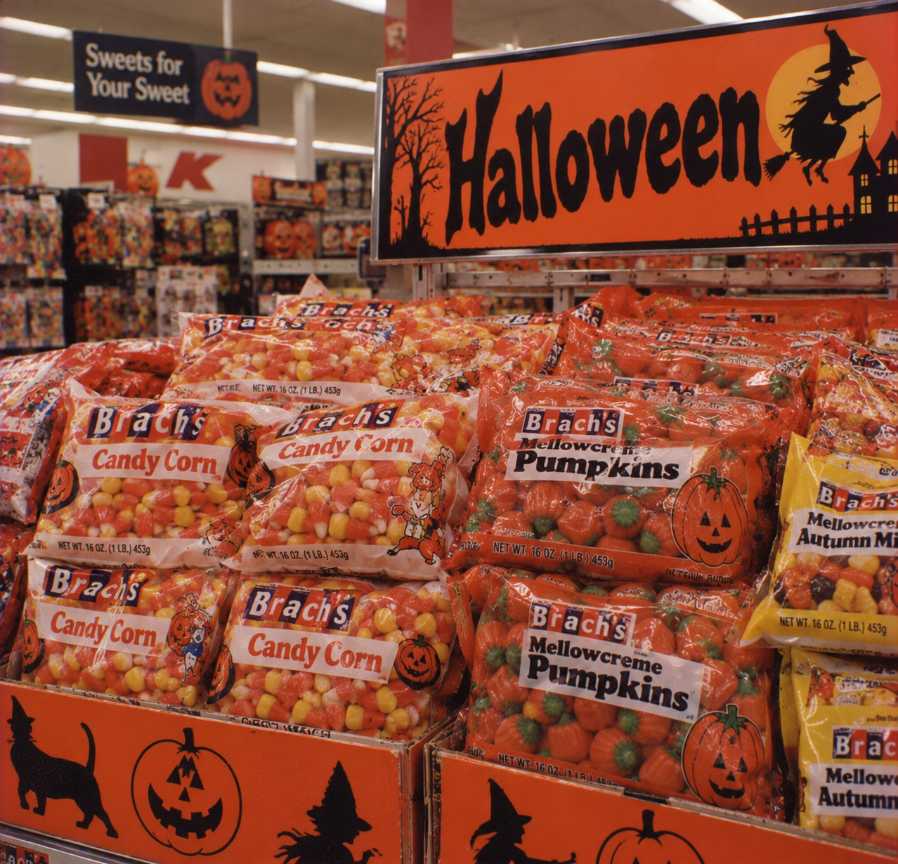Display of Brach’s candy corn and mellowcreme pumpkins in a store aisle under a large Halloween sign featuring a witch silhouette.