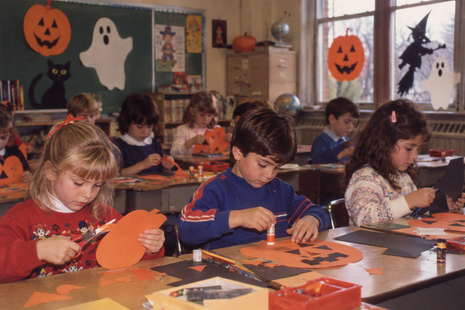 Elementary students sit at desks cutting and gluing construction paper to create Halloween decorations in a decorated classroom.
