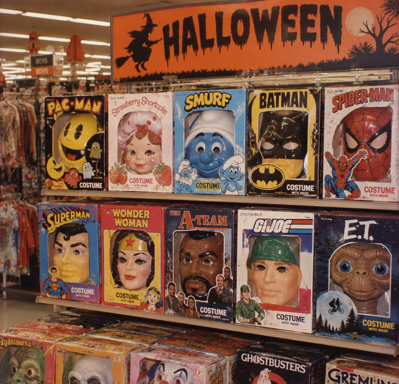 Store shelf displaying various vintage Halloween costume boxes with masks, featuring characters including Pac-Man, Batman, Spider-Man, Superman, Wonder Woman, Mr. T, G.I. Joe, and E.T. 1980s Halloween store displays.