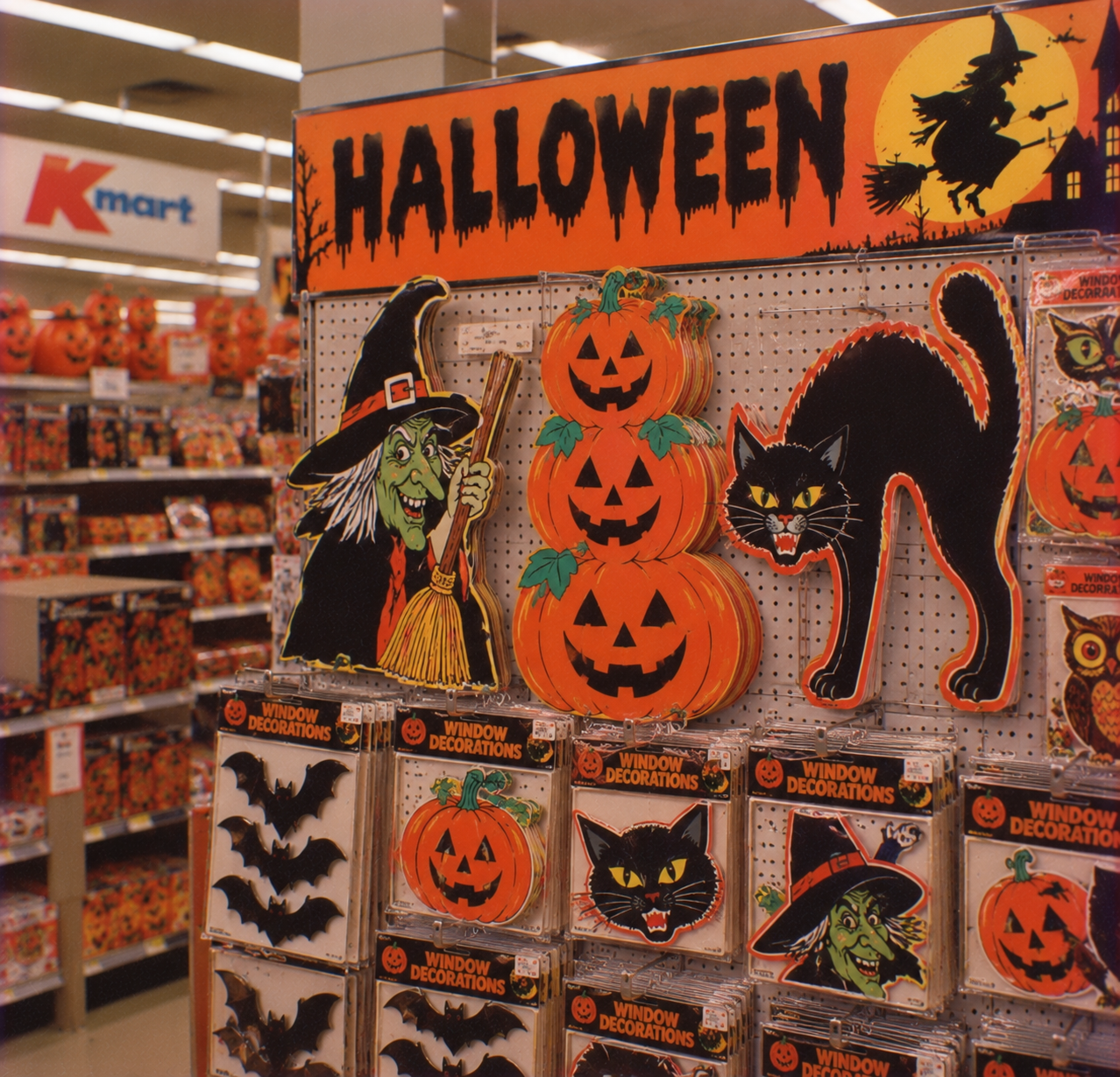 Halloween store display featuring die-cut cardboard decorations of a witch, jack-o’-lanterns, and a black cat, with packaged window decorations hanging below.