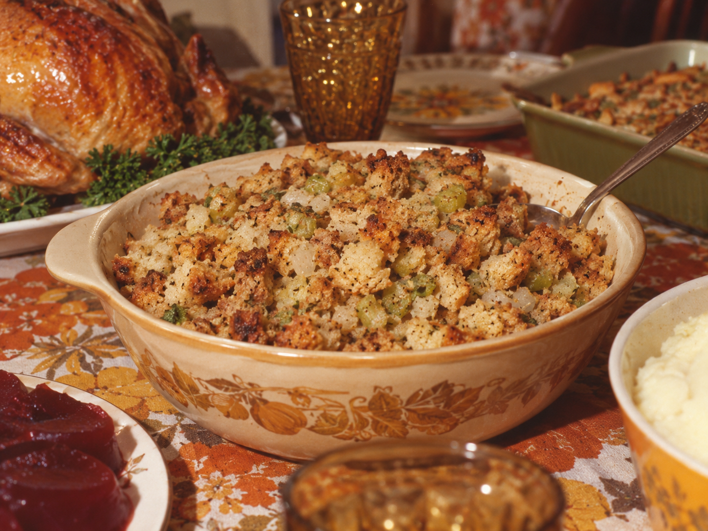 A ceramic bowl filled with stuffing on a holiday table set with a roasted turkey, mashed potatoes, and cranberry sauce. Thanksgiving dinner in 1971.