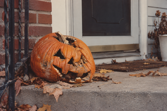 A decaying jack-o’-lantern sits on a concrete porch steps surrounded by fallen leaves.