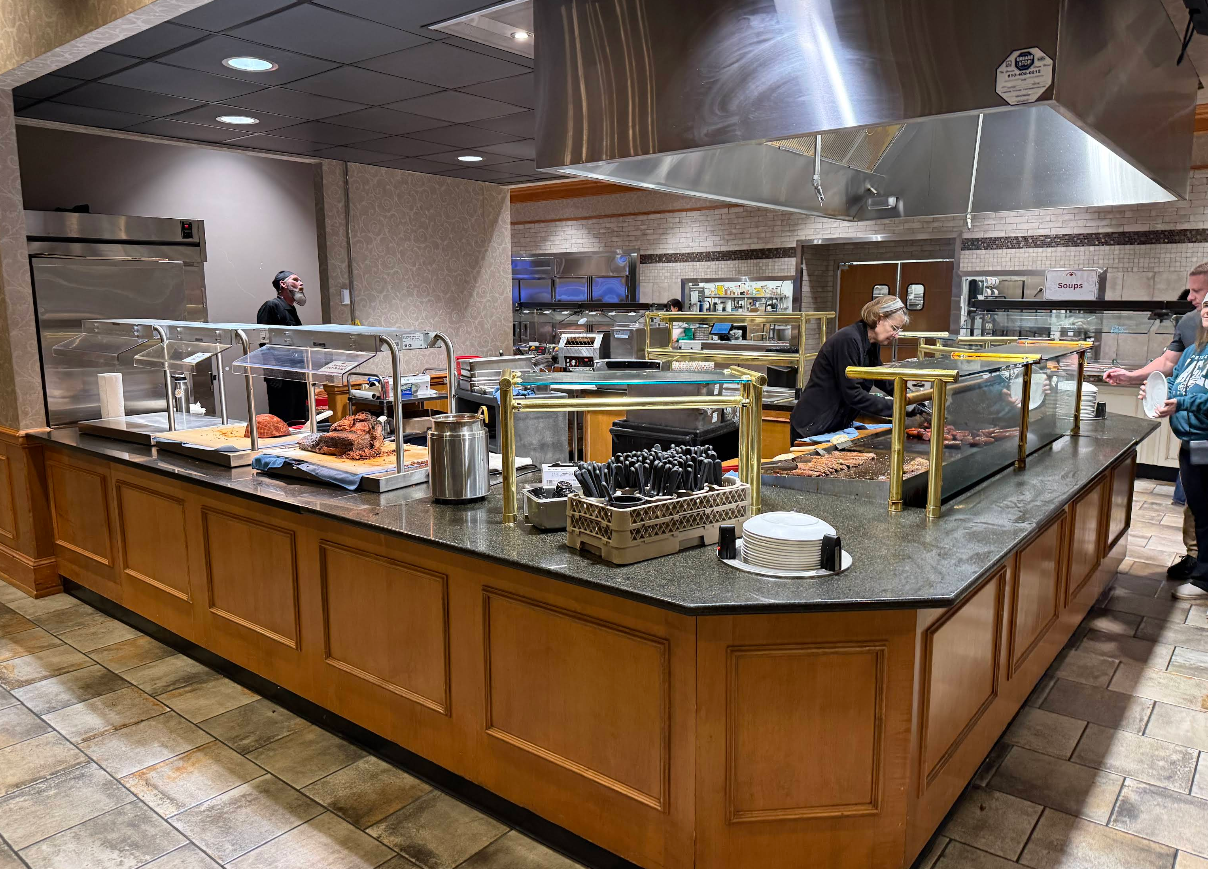 Buffet service area with a large island counter, staff preparing food, and serving stations with hot plates and serving utensils.