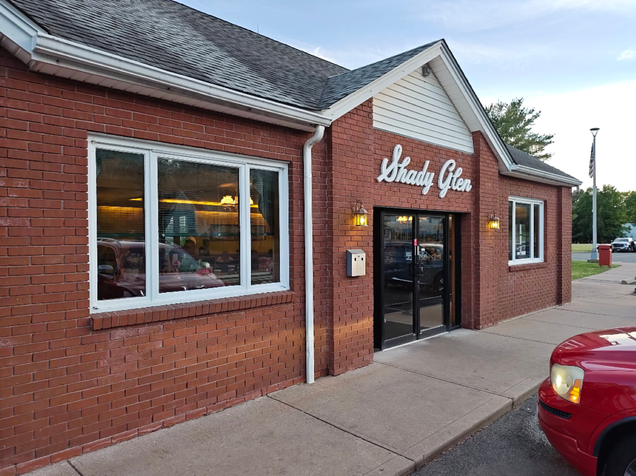 The exterior of the Shady Glen restaurant, featuring a red brick facade, large windows, and a glass front door with the name in white script lettering.