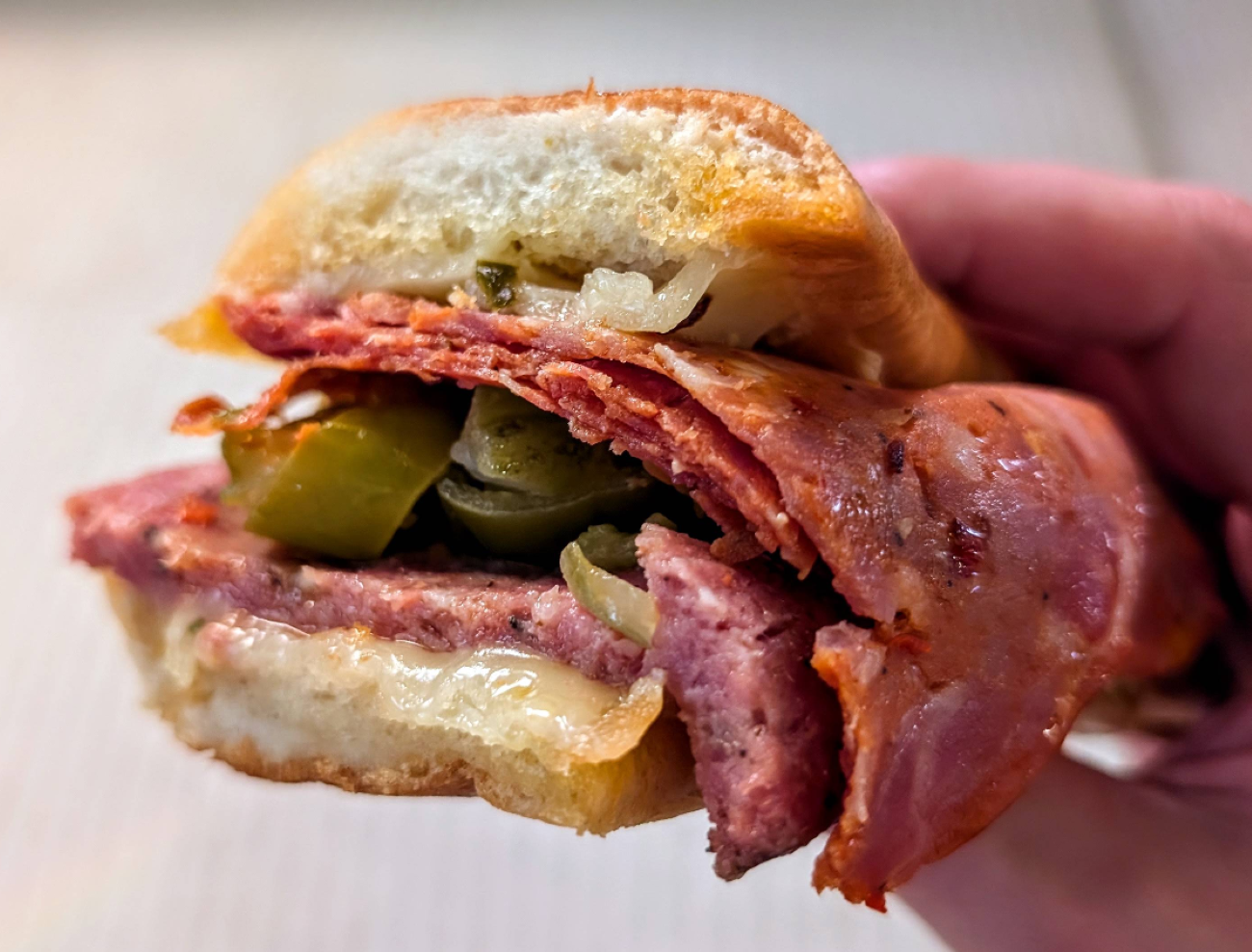 A hand holding a toasted sandwich filled with layers of sliced deli meat, melted cheese, and pickles from one of the restaurants across the USA known for next-level hoagies.