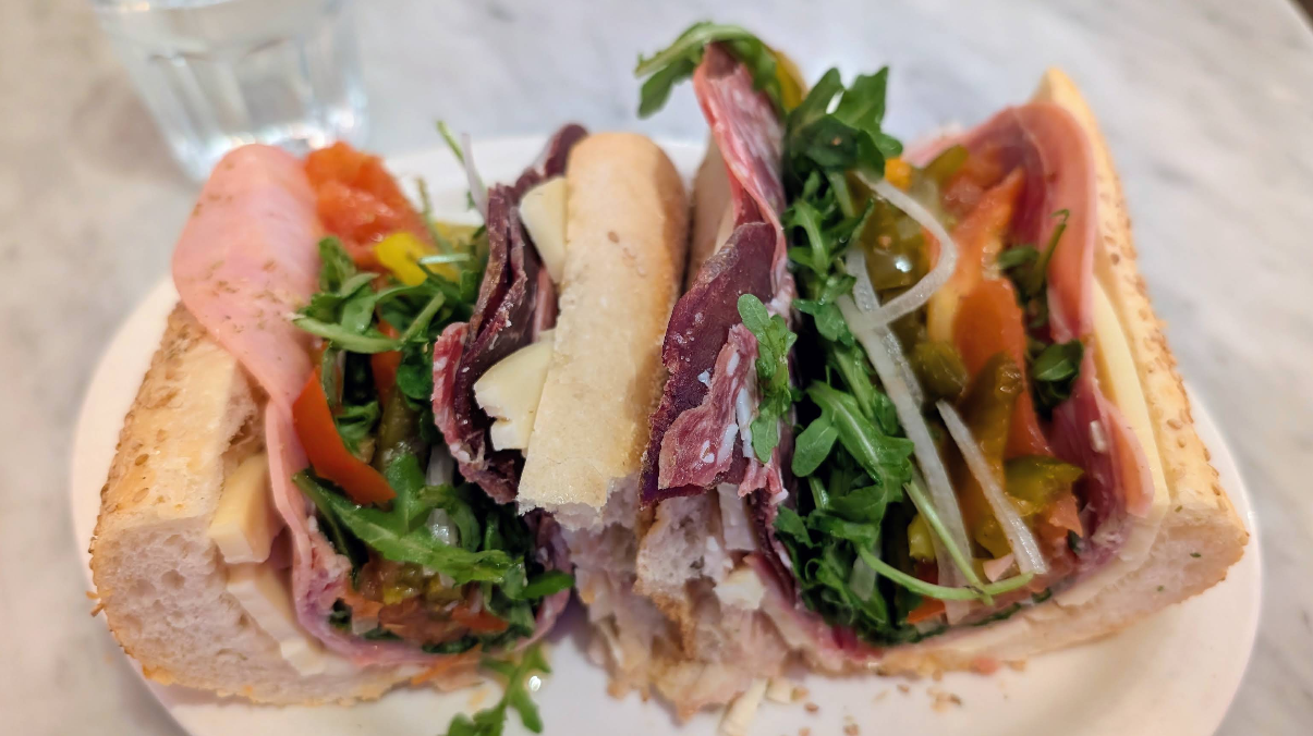 Two halves of an Italian sub sandwich—a standout among restaurants across the USA known for next-level hoagies—served on a plate with layers of deli meats, cheese, arugula, and pickled peppers on a crusty roll.