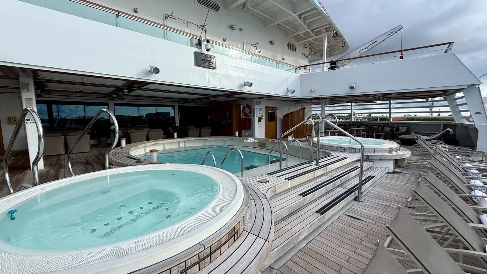 Two tiered whirlpool hot tubs on a wooden cruise ship deck with rows of empty lounge chairs.