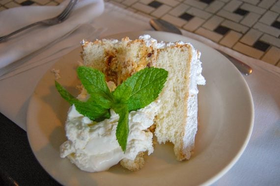 A slice of white regional dessert cake topped with whipped cream and a mint sprig on a white plate.